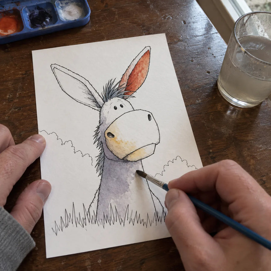 Donkey coloring page partially painted in watercolor on a wooden table.